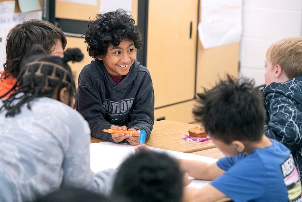 Students sitting around a table working together, using respectful language, and smiling