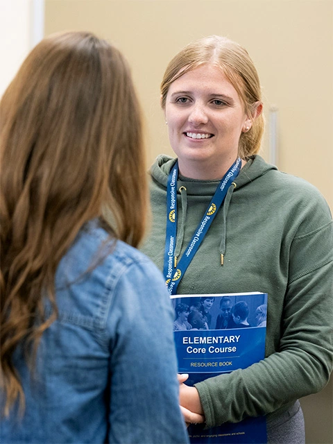 Elementary school teachers hold their resource books while participating in an activity during Responsive Classroom Elementary Core Course training.